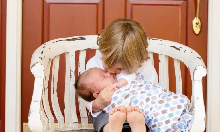 Ein Kleinkind sitzt auf einer Bank und hält ein schlafendes Baby im Arm.