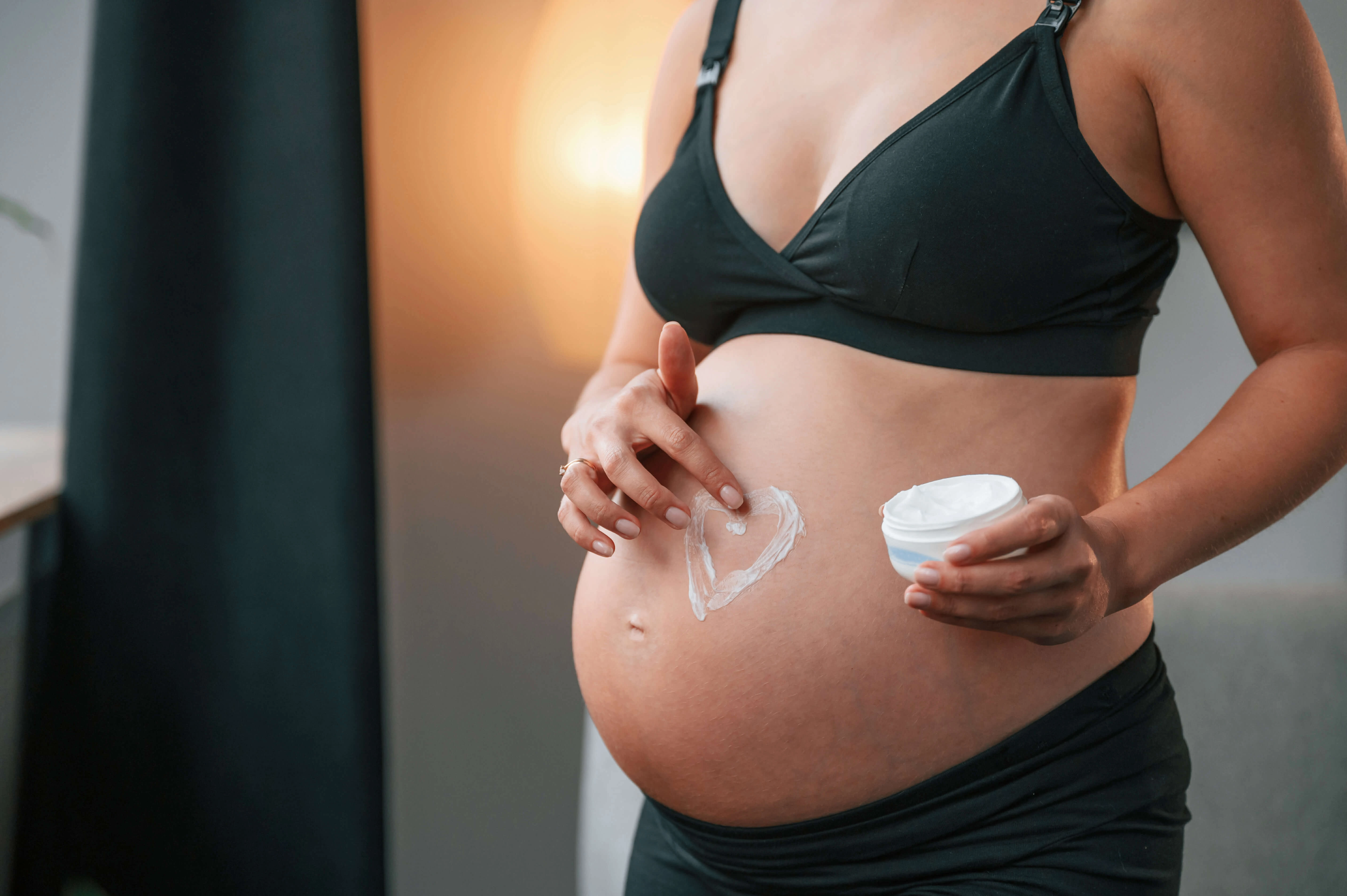 schwangere frau cremt den babybauch ein