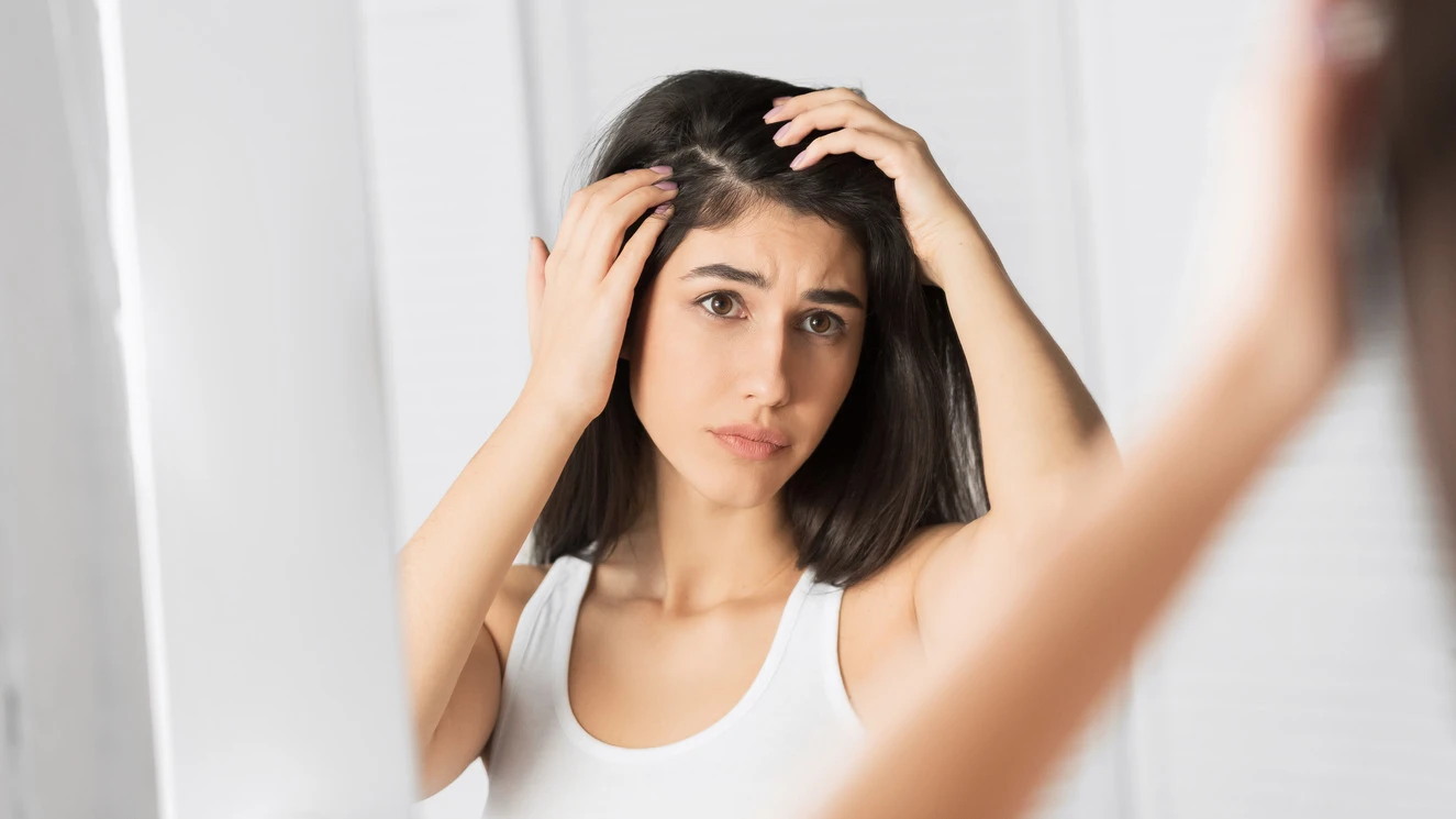 Frau schaut besorgt in den Spiegel und betrachtet ihre Haare und Kopfhaut. Akne und Haarausfall können unter anderem im Zusammenhang mit PCOS auftreten.
